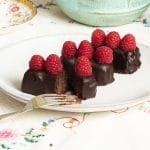 vegan chocolate ganache covered brownie bars topped with raspberries on a plate being cut into with a fork.