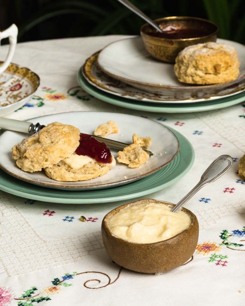 vegan clotted cream in a bowl next to a vegan scone with jam and the clotted cream inside.