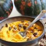 Spiced Pumpkin Hummus with a teaspoon and pumpkins in the background