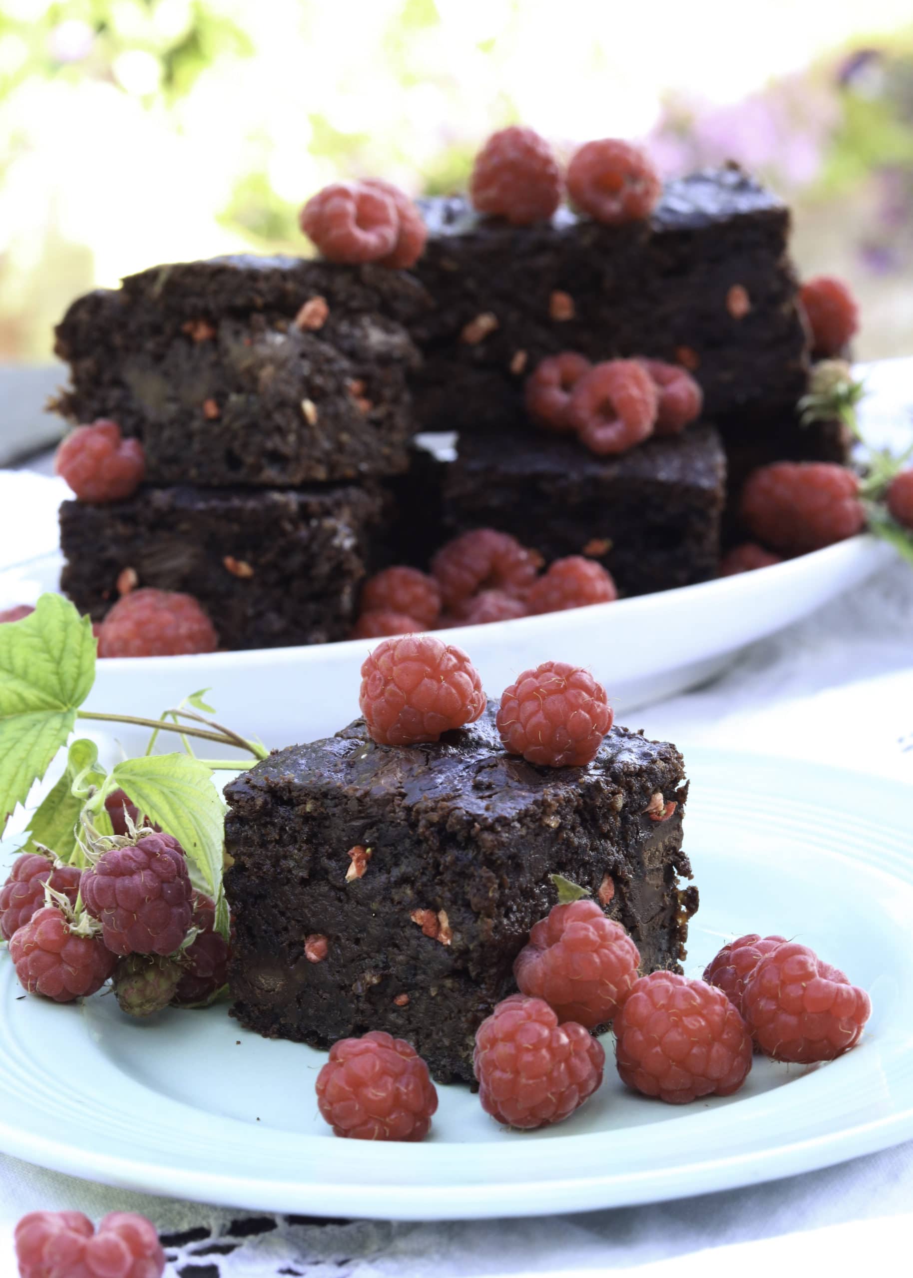 Vegan chocolate brownies on a plate topped with raspberries 