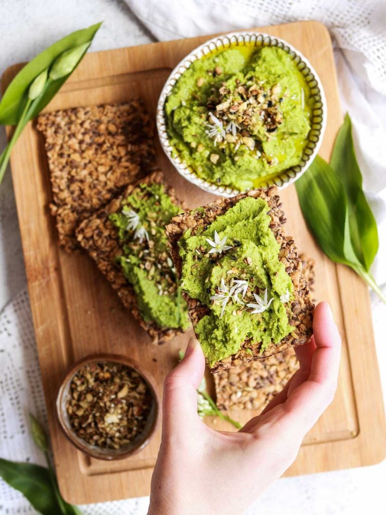 Wild Garlic Hummus on a cracker being picked up. 