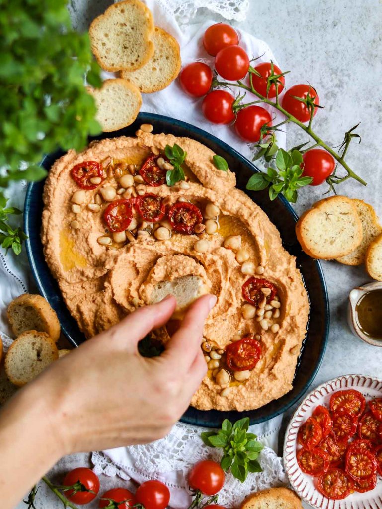 Sun Dried Tomato Hummus plate with a hand reaching down to dip some hummus up onto a cracker.