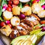 Plate of vegan peri peri chicken cut up with bbq corn on the cob and salad around it.
