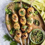 Grilled baby potatoes on a plate with lots of green salsa on top.