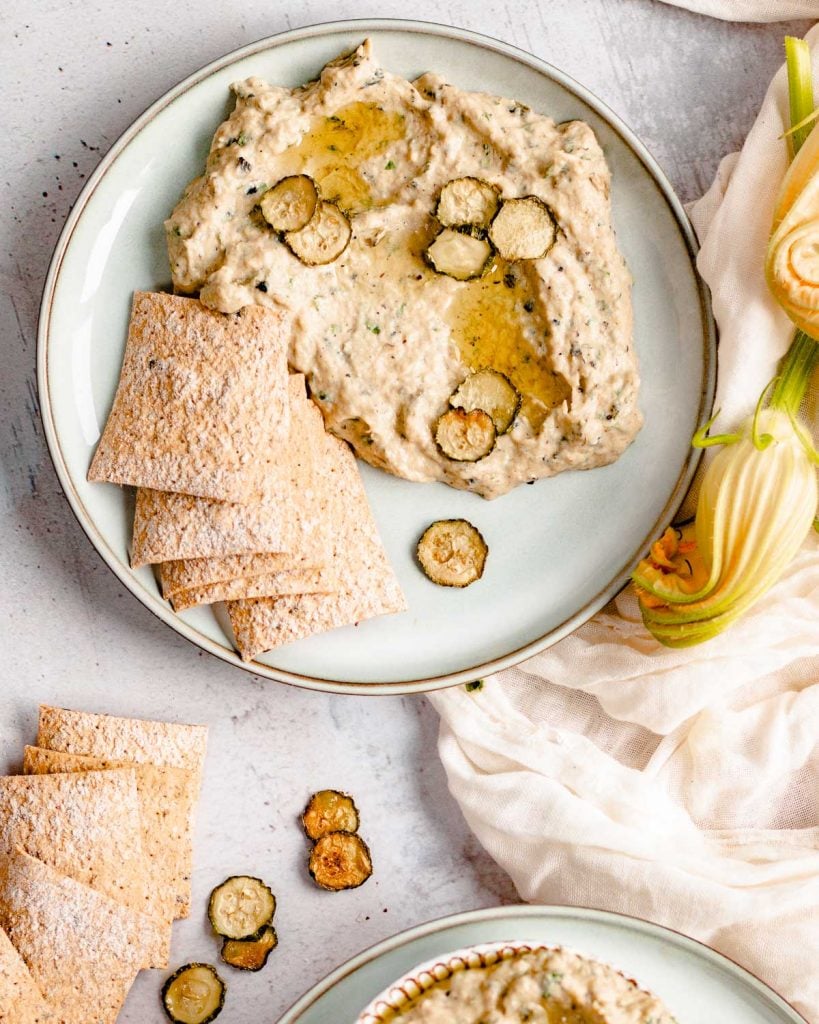 A plate of zucchini babaganoush with crackers next to it.