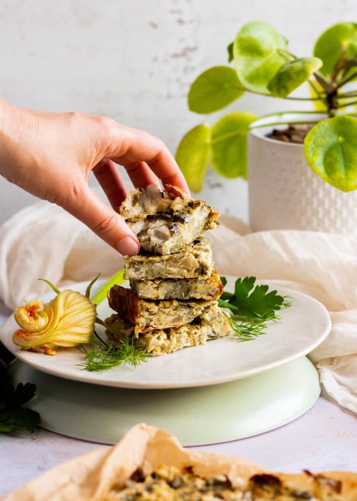 A hand reaches in to pick up a piece of zucchin slice off the plate.