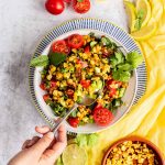 Grilled, roasted corn salad in a bowl with a hand reaching in with a spoon to scoop some up.