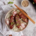 A bowl of japanese rice with miso aubergine laid on top. There are sesame seeds, radish and spring onions to garnish.