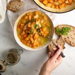 A bowl of swede and carrot soup with a hand scooping up a spoon of soup.