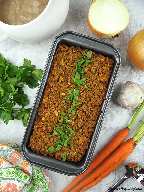 Vegan lentil loaf in a tin with herbs on top.