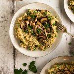 A plate of mushroom and pea risotto with extra sauteed mushrooms on top.