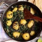 authentic vegan saag aloo curry in a dish with a wooden spoon.