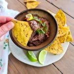Vegan Spicy black bean dip in a bowl with a hand dipping in a corn chip.