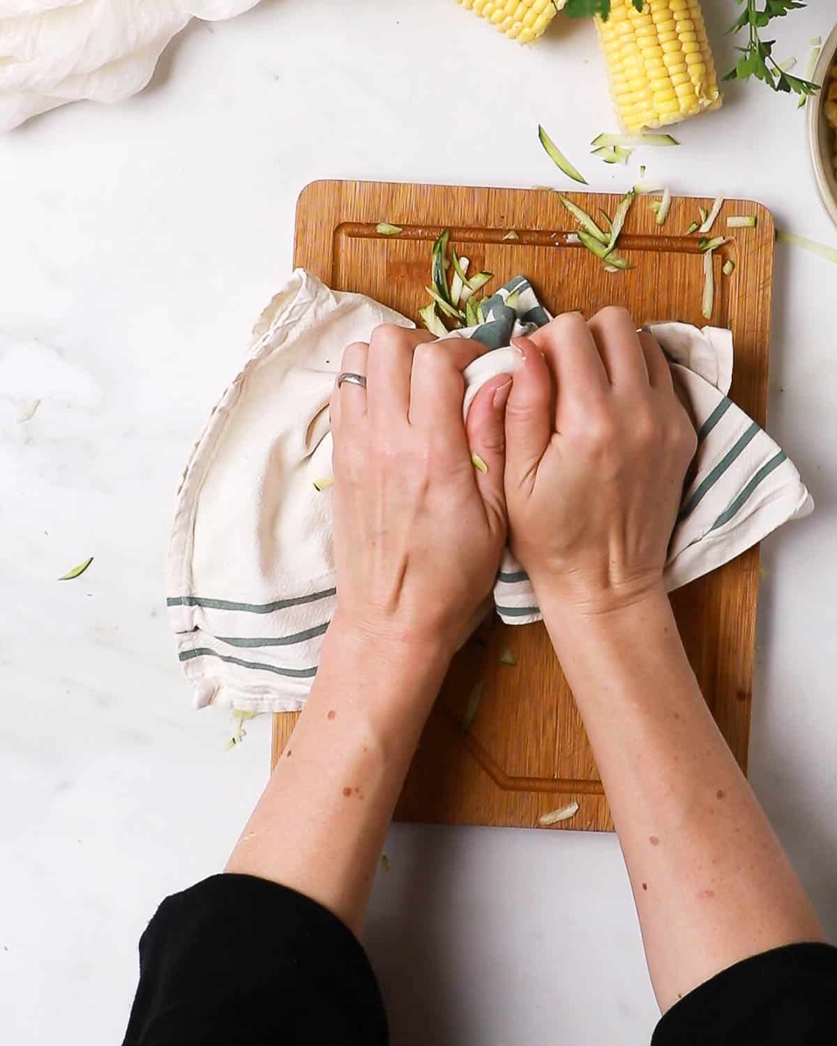 Hands squeezing the courgette in a cloth to remove moisture.
