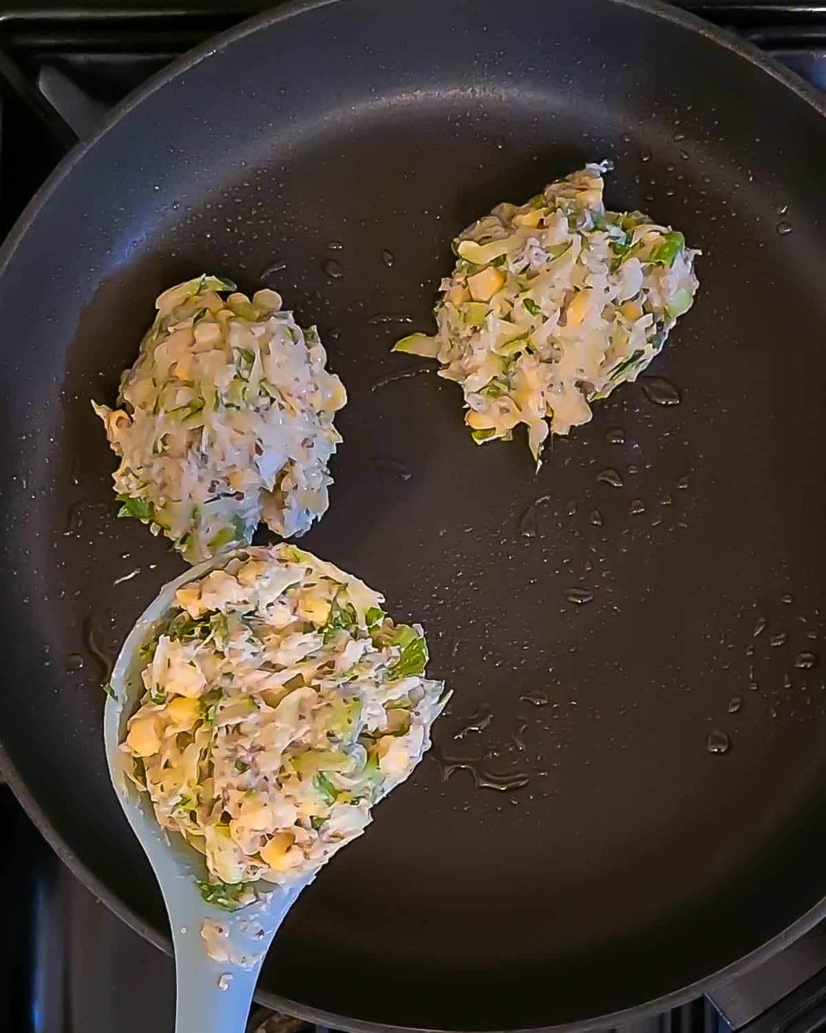 A pan with spoons of fritter mixture in it, being fried.