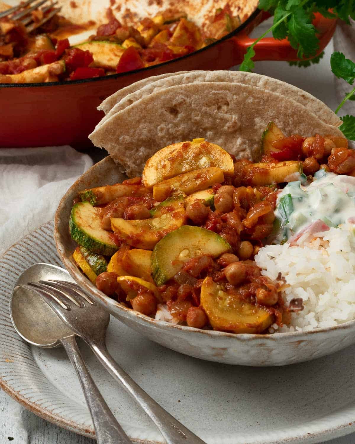 A big bowl of courgette curry with raita and rice.