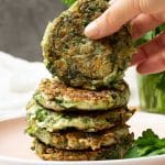 A stack of mucver (vegan zucchini fritters) with a hand reaching in and picking one up.