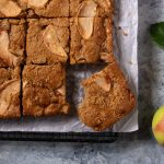 Apple cake on a cooling rack. It has been cut into pieces and a bite is taken out of one piece.