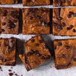 A tray of just baked vegan pumpkin brownies with a hand reaching in to pick one up.