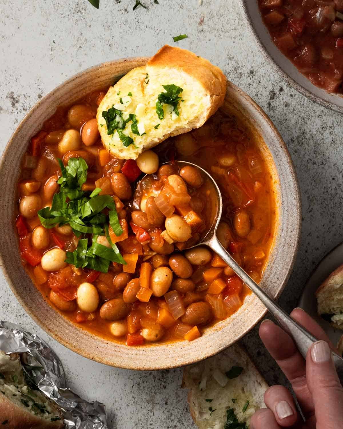 A bowl of borlotti bean stew with a spoon in it, ready to eat.