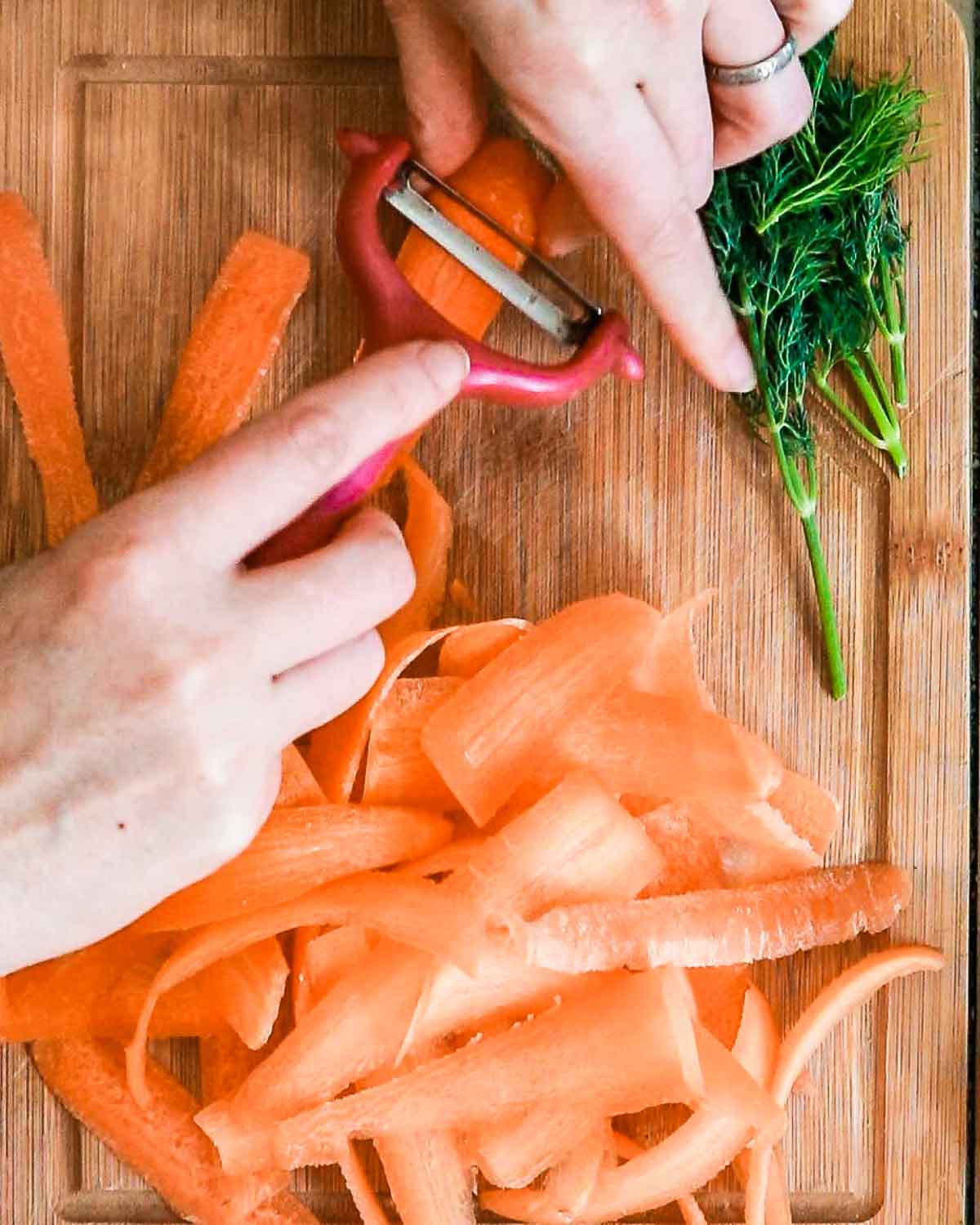 Carrots being sliced into long thin flat pieces by a vegetable peeler. 
