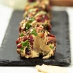 A vegan cheese ball on a platter with a little bit taken out of it.
