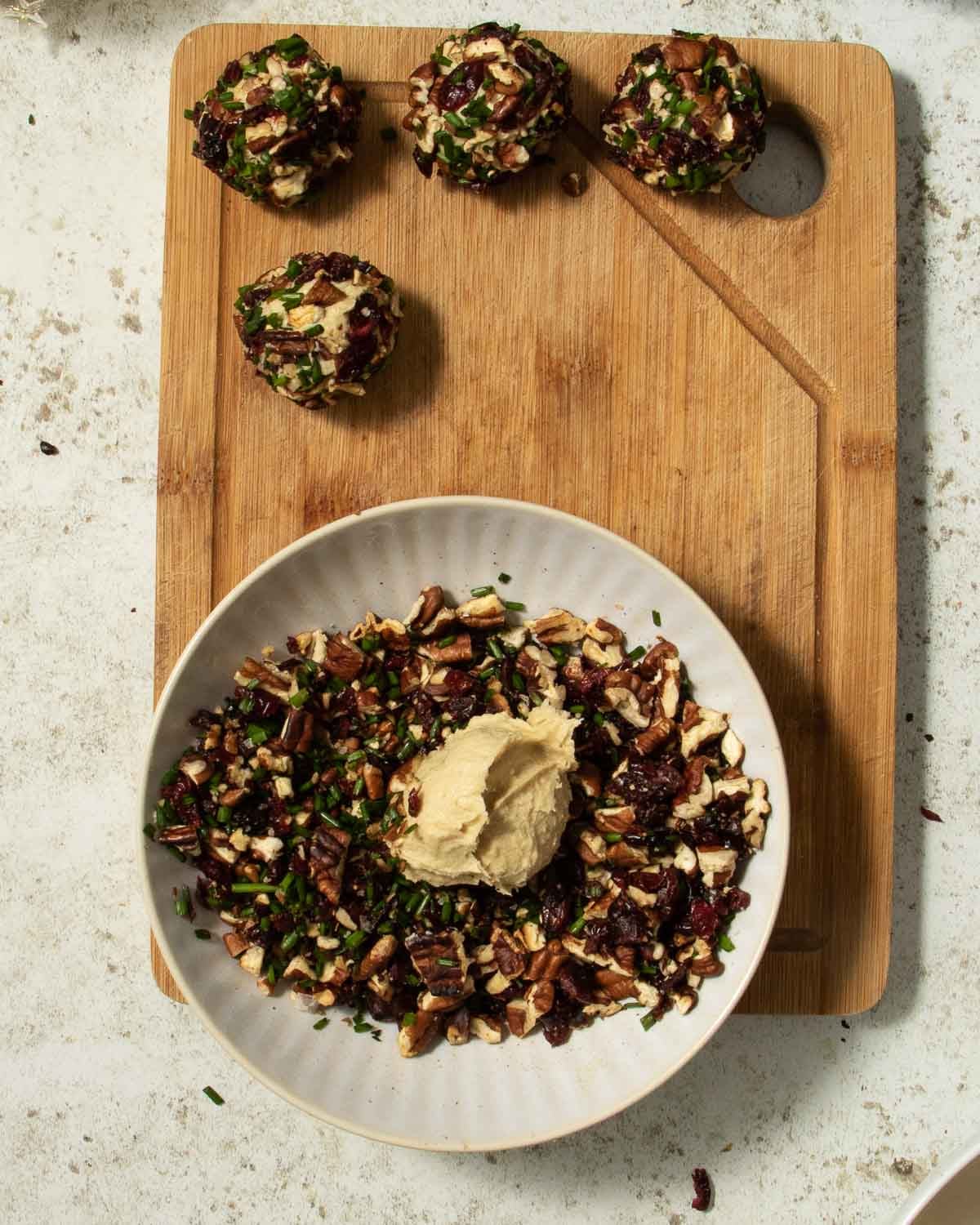 A blob of cashew cheese in a bowl with the outer cheese ball crust ingredients, ready to be rolled into balls.