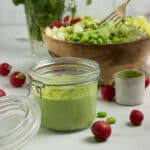 Lemon Herb tahini sauce in a jar with a salad behind it.