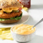 Vegan Mayo with sriracha in a little pot with a burger in the background.