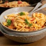 A bowl of creamy white bean pasta with tomatoes ready to eat.