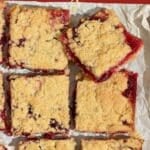 Vegan cranberry shortbread bars, with one being held up to the camera to show the juicy cranberry interior.