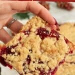 Vegan cranberry shortbread bars, with one being held up to the camera to show the juicy cranberry interior.