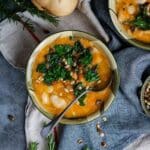 A bowl of cozy butternut squash and white bean soup with crispy kale on top, ready to eat.