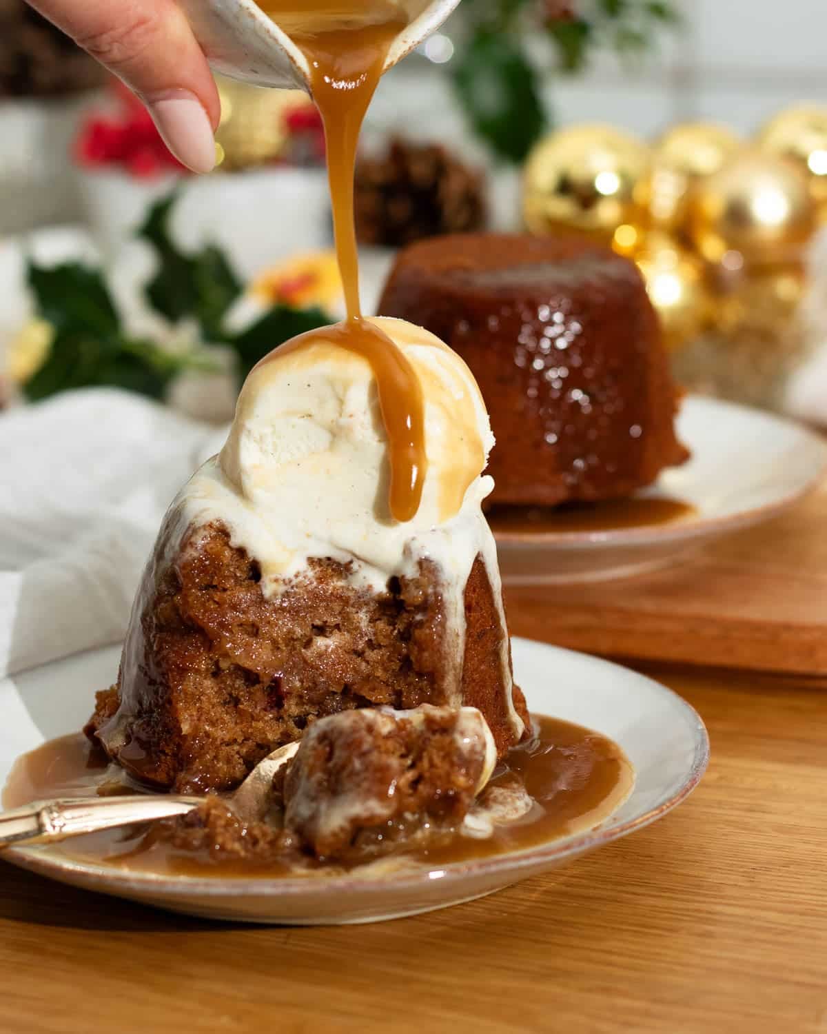 Vegan Sticky Toffee Pudding with vegan icecream and more toffee sauce being poured on top.