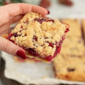 Vegan cranberry shortbread bar being held up to the camera to show off the crumble topping and pretty cranberry filling.