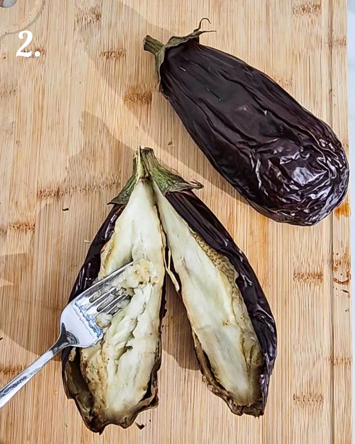 Cutting the roasted eggplant in half and scooping out the cooked inner flesh.