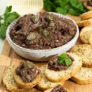 Eggplant tapenade in a little bowl ready to eat. There are some crostini around it with tapenade on them.