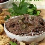 Eggplant tapenade in a little bowl ready to eat. There are some crostini around it with tapenade on them.