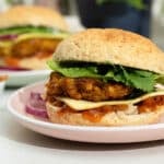 A cauliflower and chickpea burger stacked with mango chutney, lettuce and vegan cheese. There is another burger in the background.