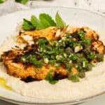 A cauliflower steak on a plate sitting on top whipped butterbeans with green salsa verde on top.
