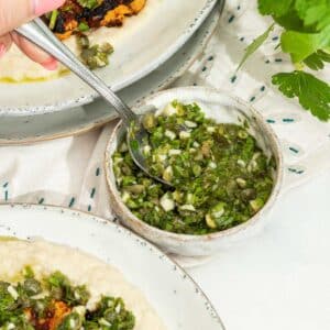 A little bowl of caper, herb and lemon salsa verde with some cauliflower steaks in the background.