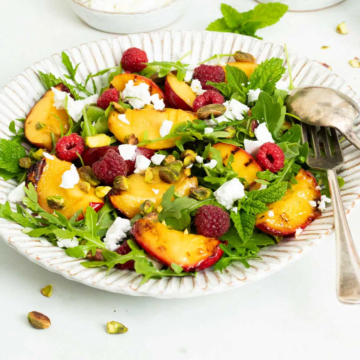 A plate of salad with grilled nectarines, arugula (rocket salad), raspberries and pistachio nuts.