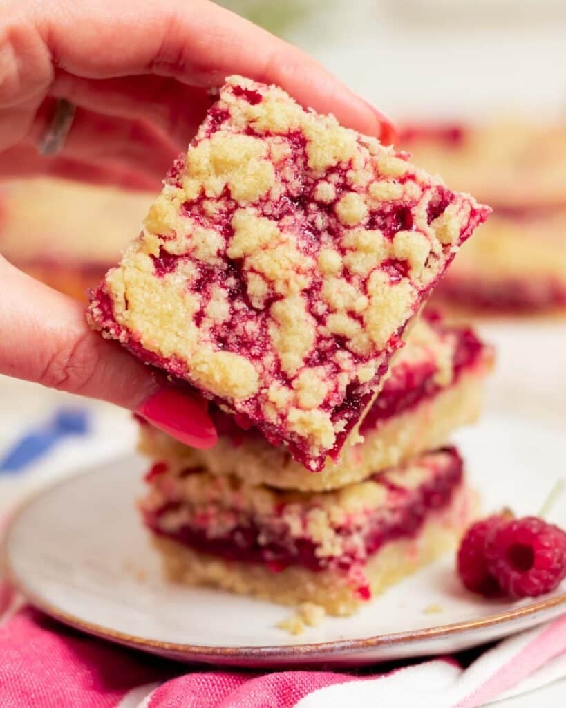 Close up of the raspberry shortbread bar ready to eat, with a hand holding it up.