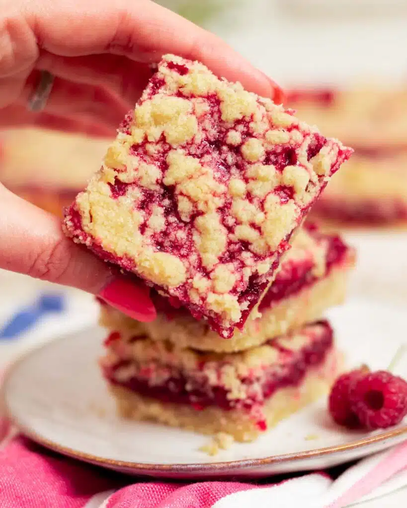 Close up of the raspberry shortbread bar ready to eat, with a hand holding it up.