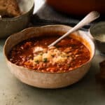 A bowl of lentil and tomato soup with some vegan cheese sprinkled over it, ready to serve.