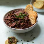 A bowl of sundried tomato and olive tapenade with crackers ready to eat.