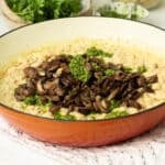 A pan of creamy white beans with pan roasted mushrooms and pesto on top.