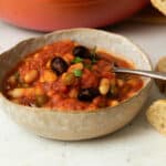 A bowl of white bean puttanesca with a few olives on top ready to eat.