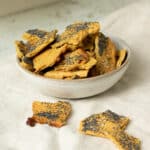 Cheesy Chickpea flour crackers in a bowl. The crackers are topped with poppy seeds.
