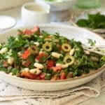 A plate of white bean salad with peppers and olives with some smaller plates and extra dressing in a pot in the background.